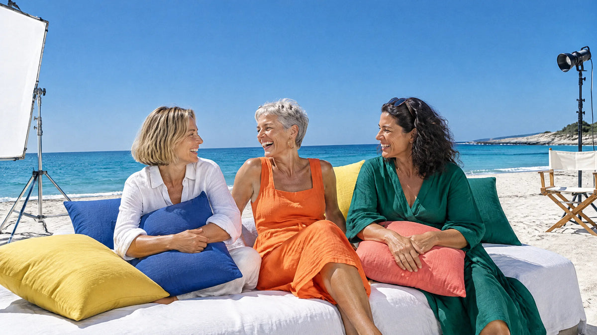 Three women laughing on a beach daybed with colourful cushions during a photoshoot